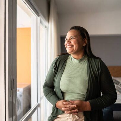 Happy mature woman contemplating at home A woman standing in front of a window.