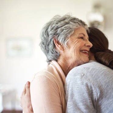 Shot of a senior woman hugging a young nurse in a retirement home A woman hugging another person in a room.